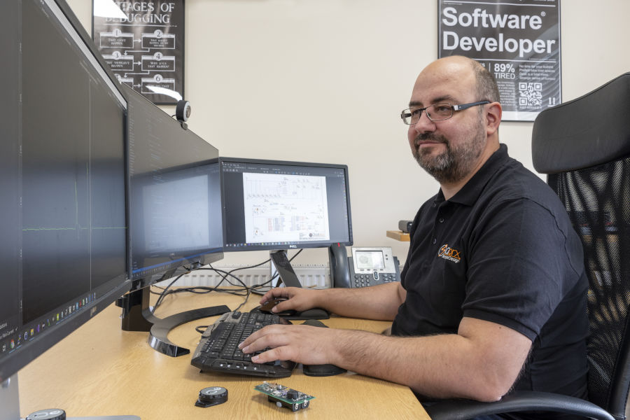 Software engineer writing code at computer with three monitors